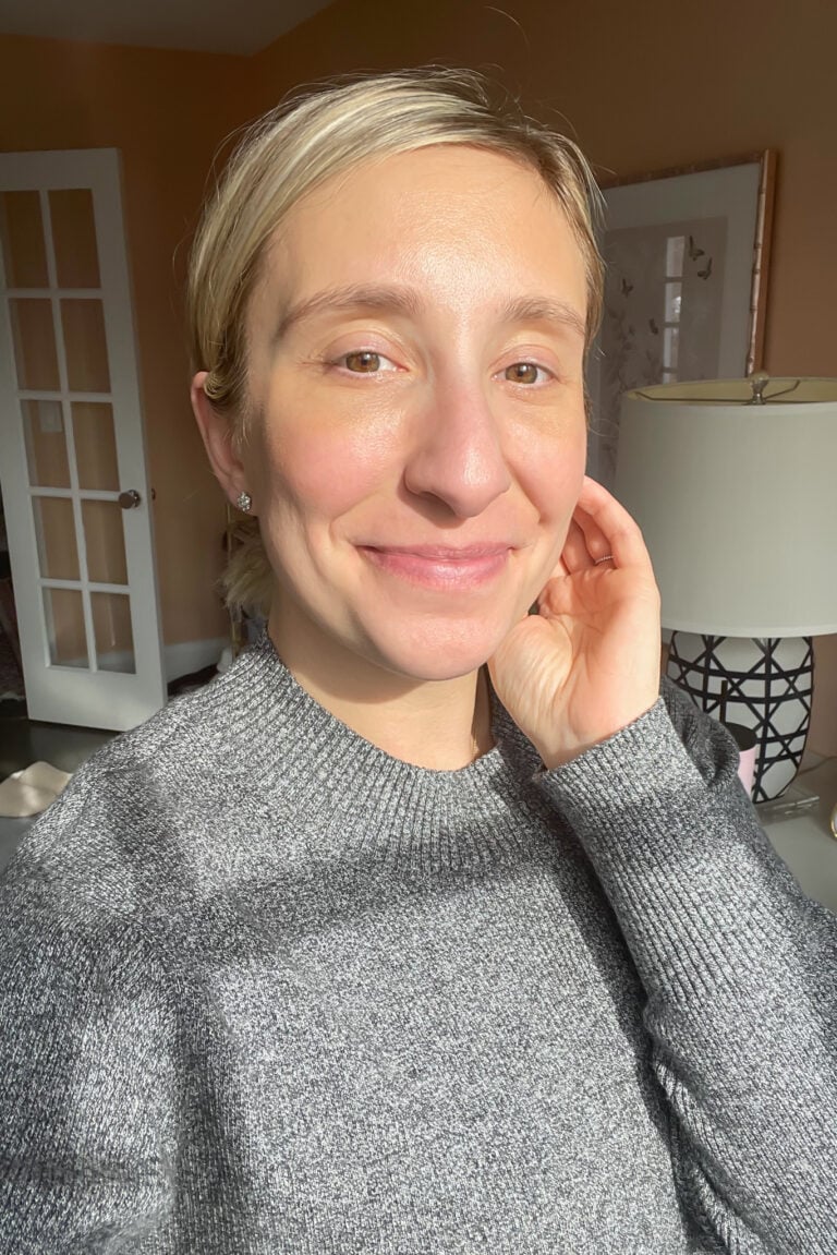 Woman with glowing skin wearing a gray sweater after using Vintner’s Daughter skincare products in a natural light selfie.