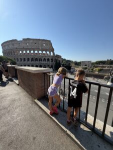 Two kids leaning on a railing looking out at the Colosseum while traveling to Europe with kids