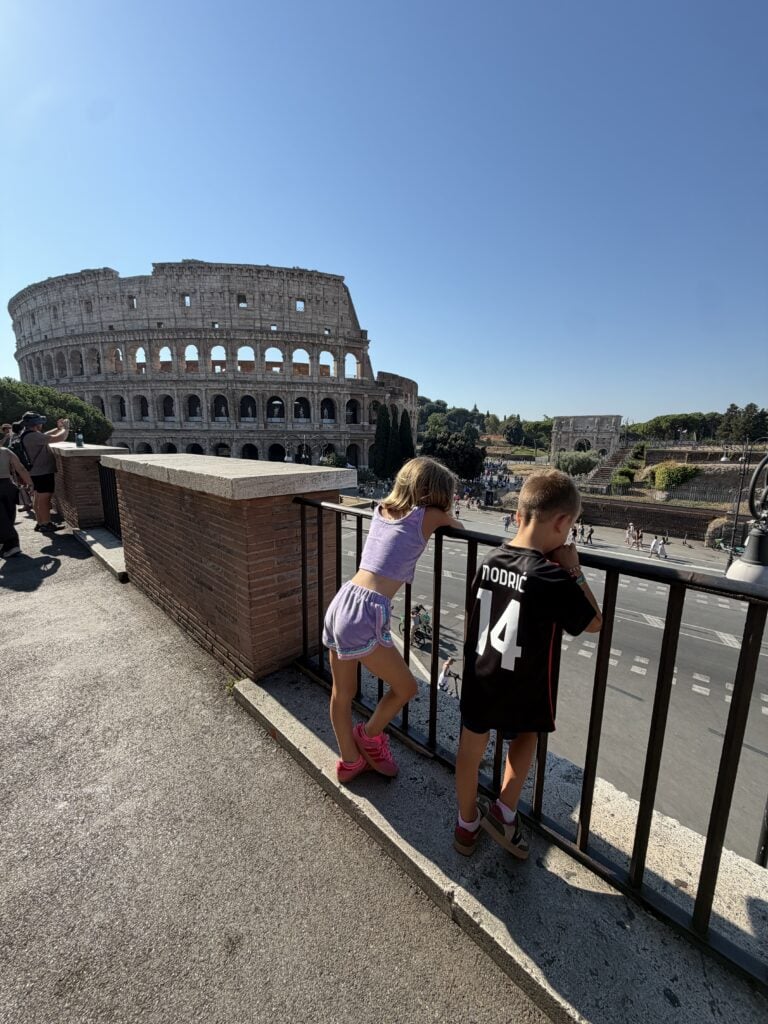 Two kids leaning on a railing looking out at the Colosseum while traveling to Europe with kids