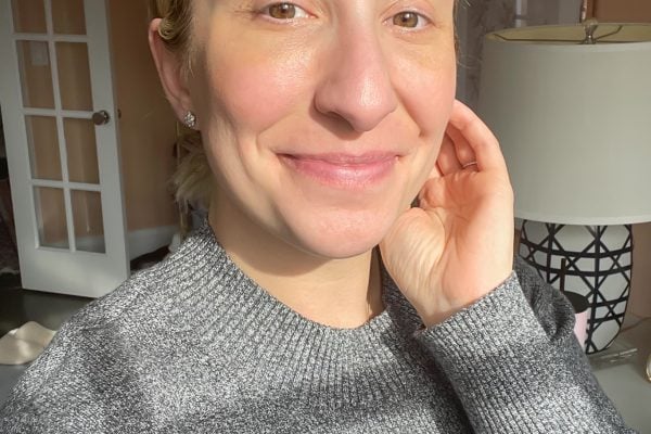 Woman with glowing skin wearing a gray sweater after using Vintner’s Daughter skincare products in a natural light selfie.