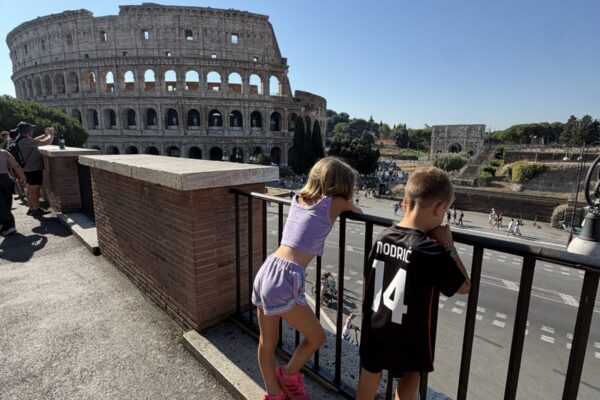 Two kids leaning on a railing looking out at the Colosseum while traveling to Europe with kids